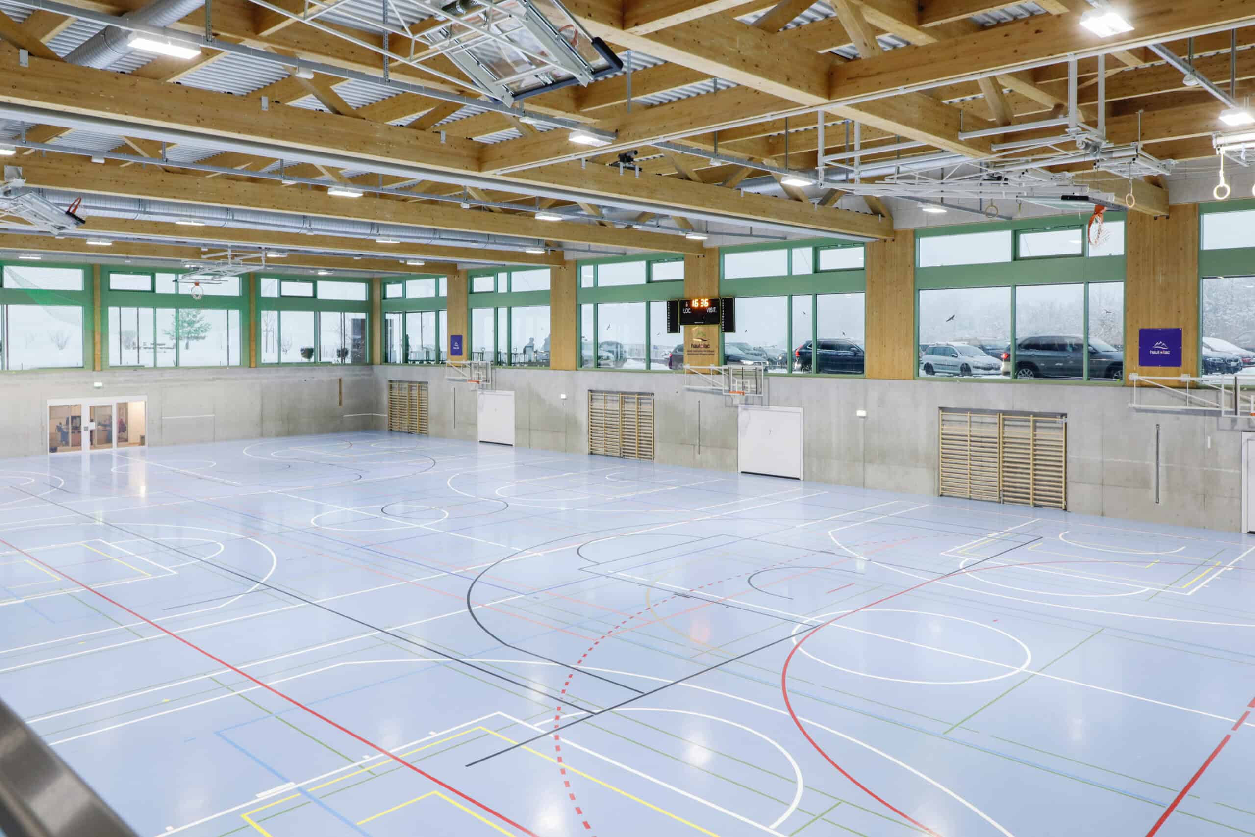 Bright indoor sports hall with wooden beams and large windows, ideal for school athletic facilities.