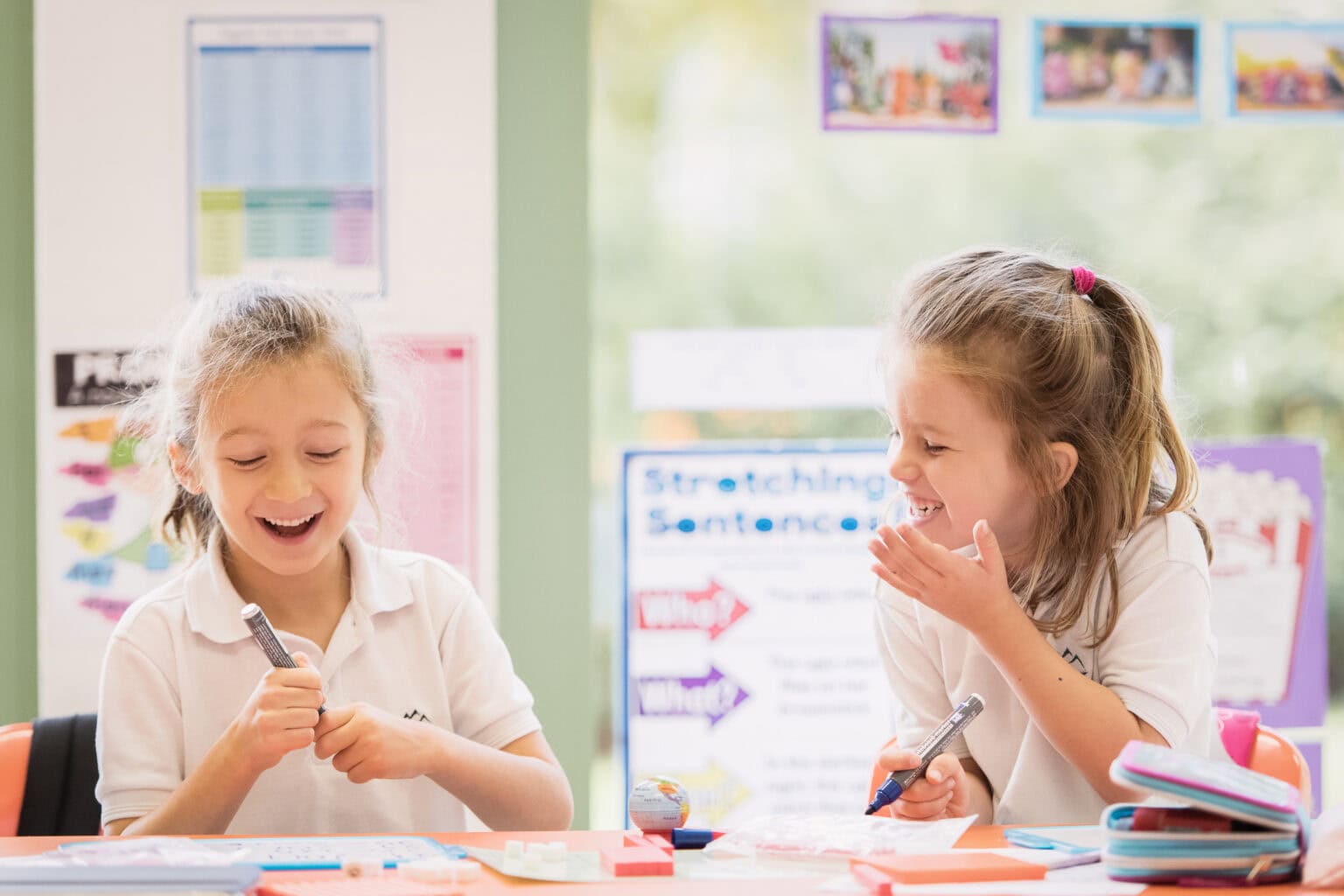 Young schoolgirls laughing and having fun in a classroom during an educational activity.