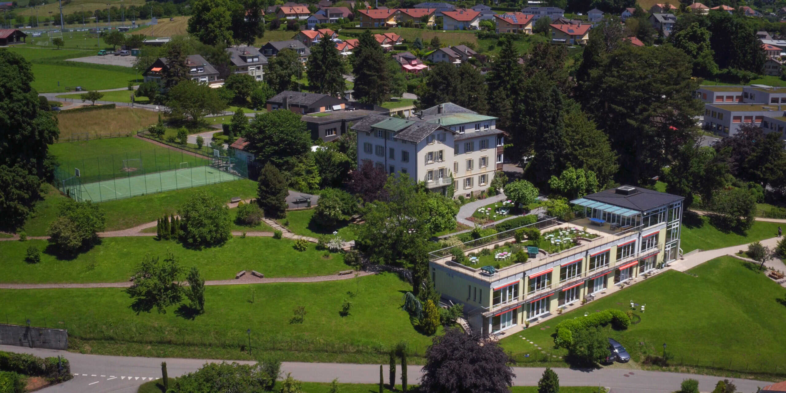 Spacious school campus with lush greenery, sports facilities, and modern buildings for student activities.