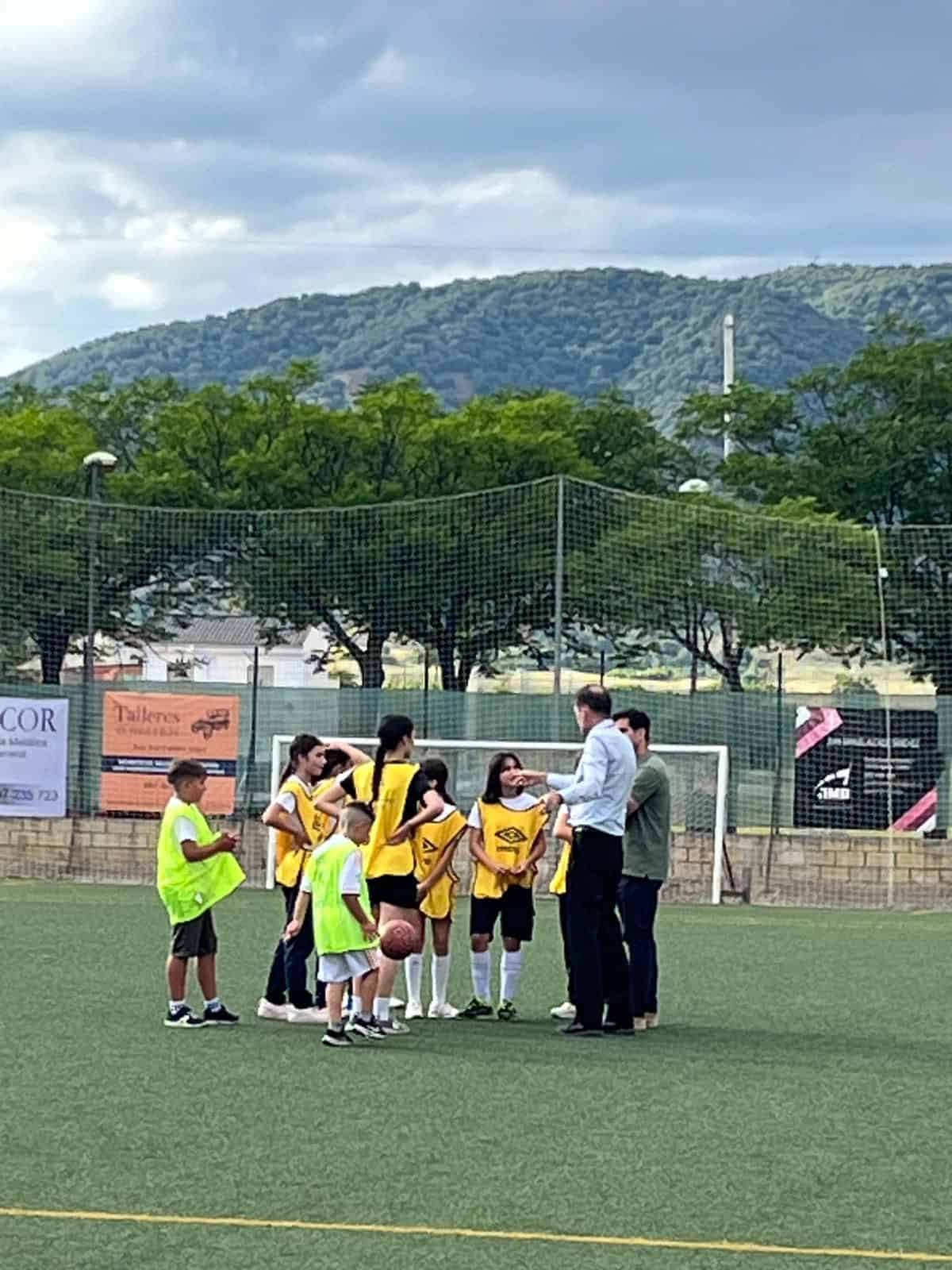 Group of children and coach practicing sports on school field outdoors.