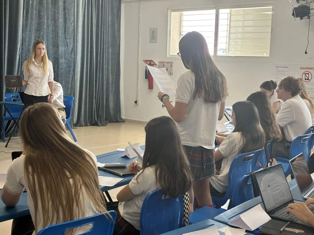 Students in a classroom engaging in a lesson with a teacher at the front.