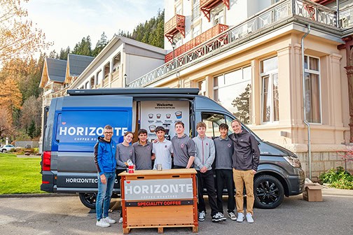 Students Experience Entrepreneurship with Impact Through Local Coffee Partnership 6 Mobile coffee stand with young students in front of a school building, promoting quality education.