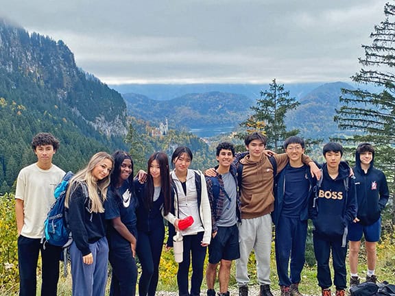 A diverse group of students outdoors with scenic mountains and trees in the background.