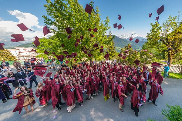 Graduates celebrating outdoors with caps flying in the air at a global school event.