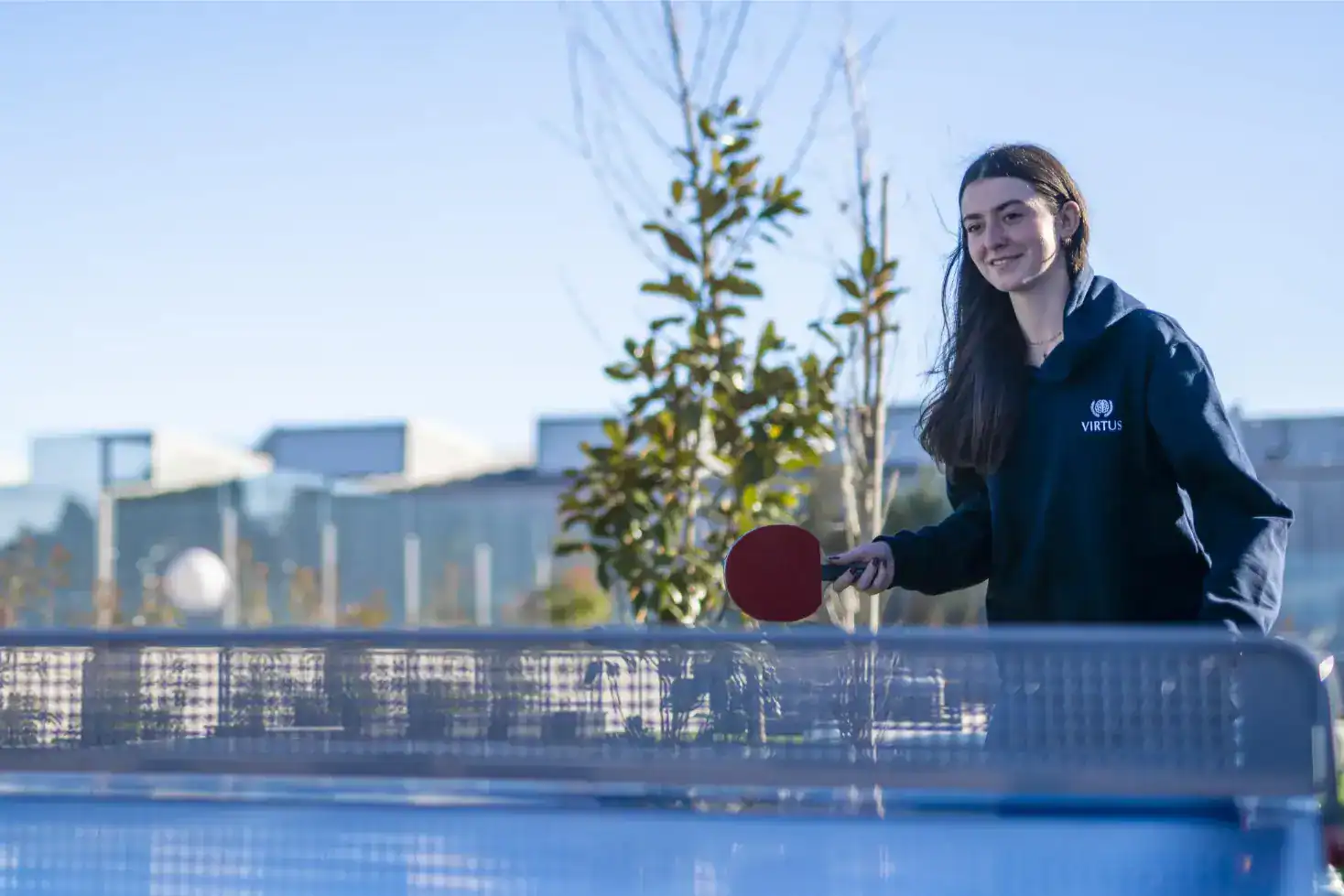 Młoda studentka grająca w tenisa stołowego na świeżym powietrzu podczas światowej imprezy sportowej dla szkół, promującej aktywne uczenie się i edukację globalną.
