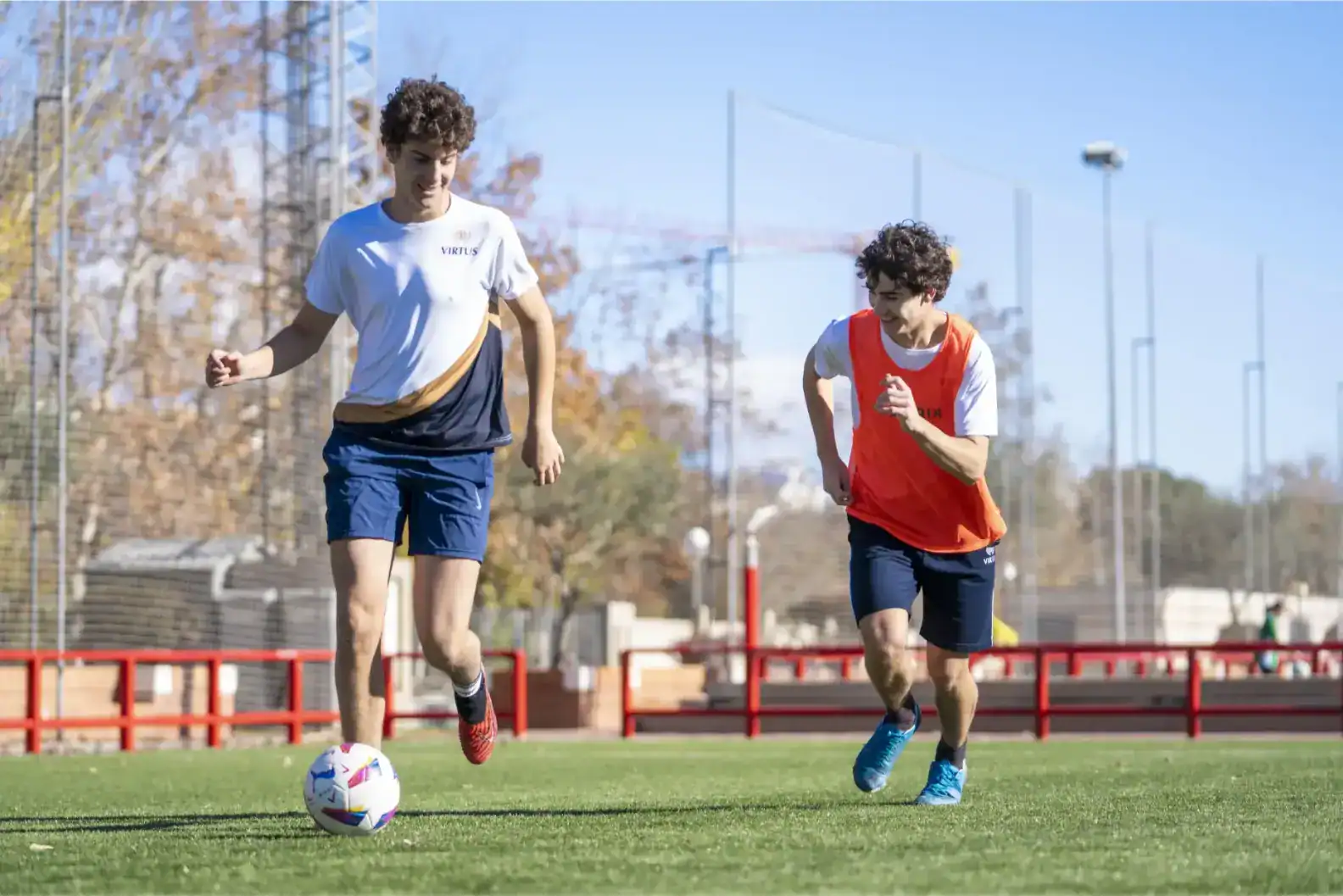 Młodzi uczniowie grający w piłkę nożną na szkolnym boisku sportowym, promujący wychowanie fizyczne i zajęcia sportowe dla uczniów.