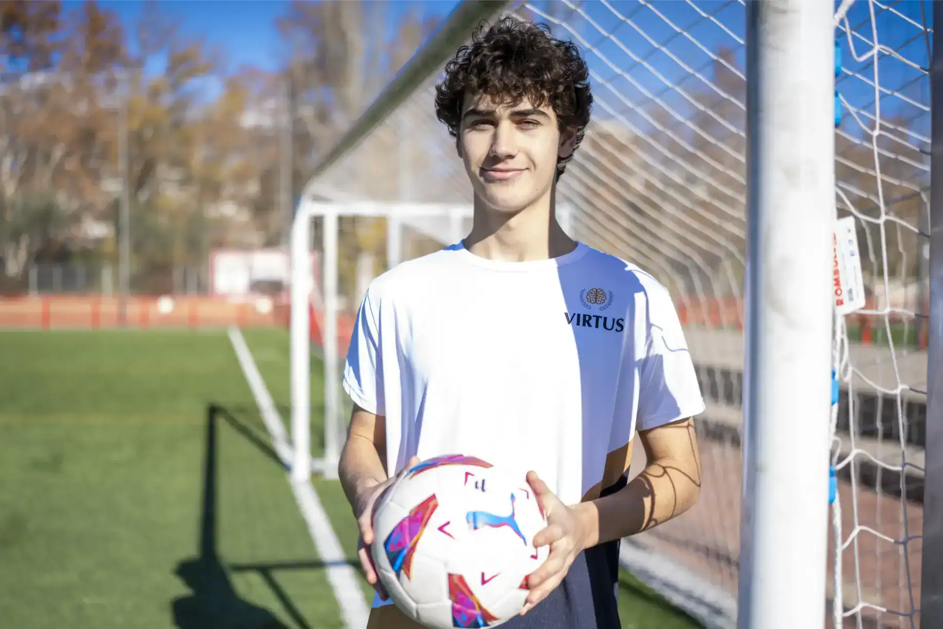 Młodzieżowy piłkarz trzymający piłkę na szkolnym boisku sportowym.