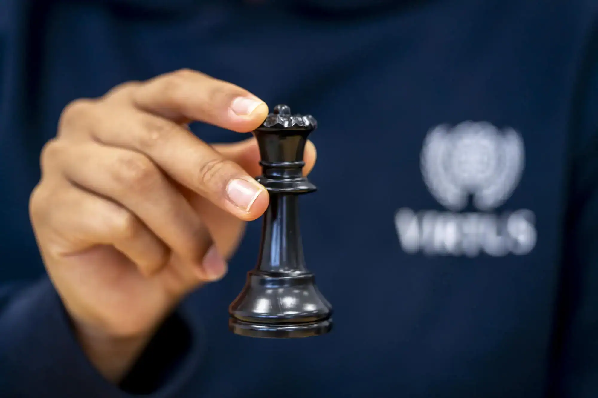 Osoba trzymająca czarną figurę szachową, symbolizującą strategiczne myślenie i edukację.