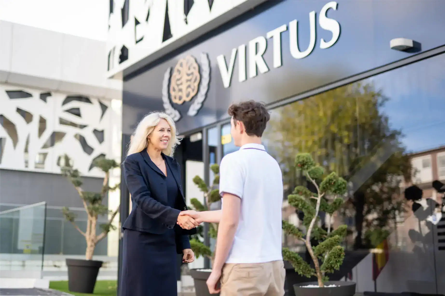 Nowoczesne wejście do szkoły w Virtus School z personelem angażującym uczniów na zewnątrz.