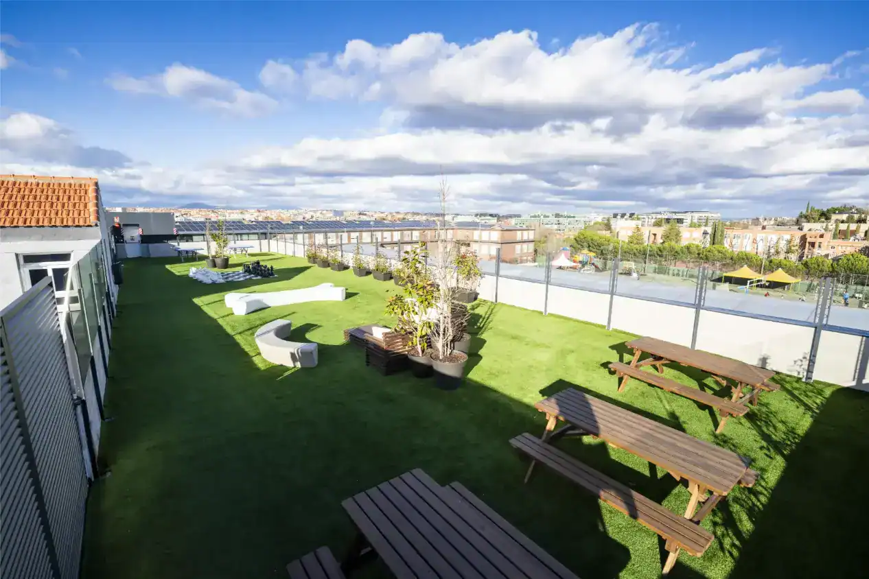 Jasna przestrzeń zewnętrzna na dachu World Schools z miejscami do siedzenia, zielenią i terenem sportowym do rekreacji dla uczniów.