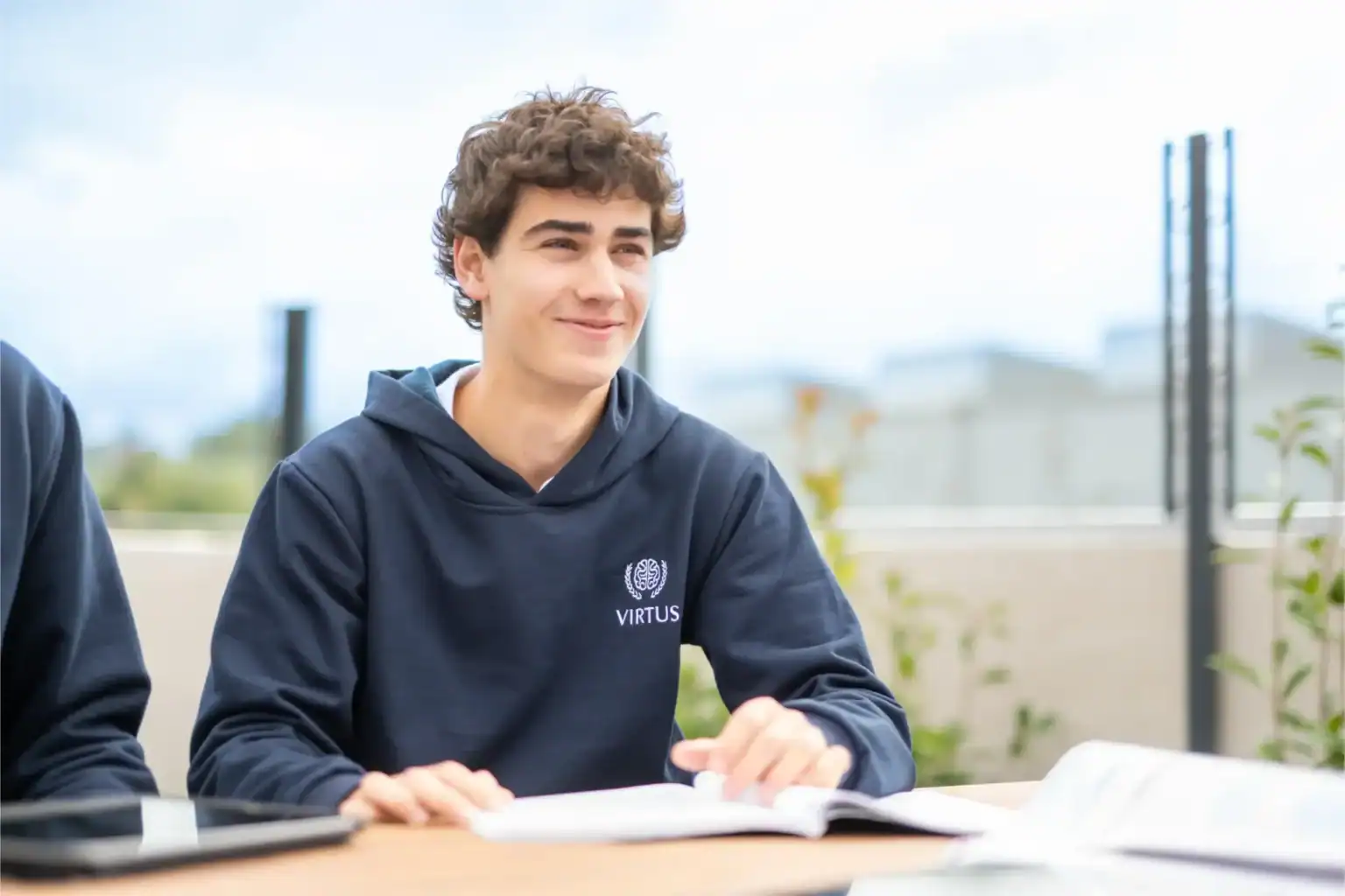 Młody uczeń w mundurku szkolnym z logo Virtus, cieszący się nauką na świeżym powietrzu, podkreślający globalną doskonałość edukacji szkolnej.