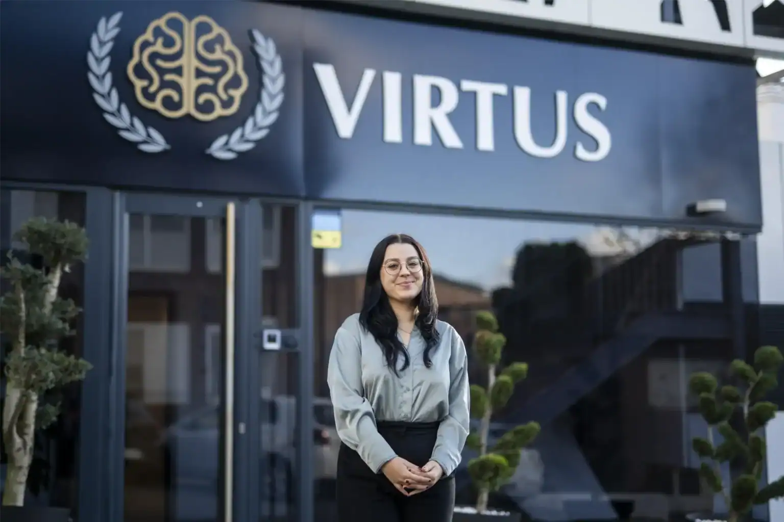 Nowoczesne wejście do szkoły ze znakiem Virtus, uczeń stojący pewnie na zewnątrz.