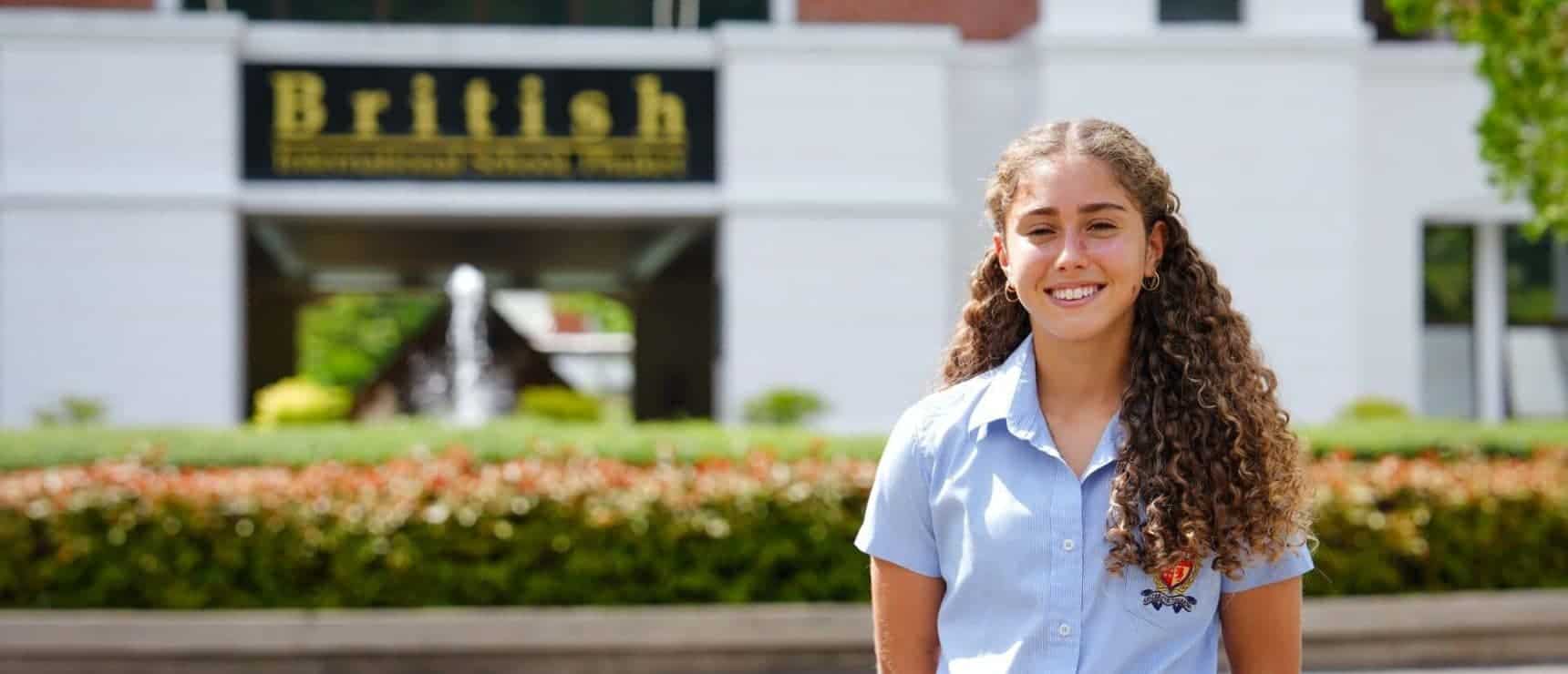 Bright smiling girl in school uniform standing outdoors in front of World Schools campus for global education.