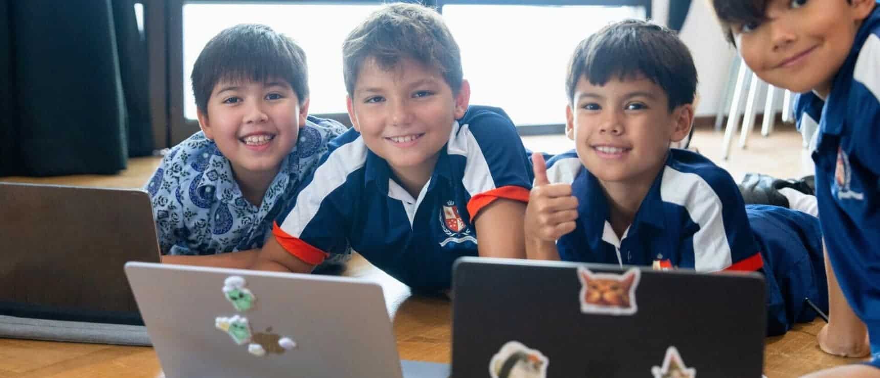 Smiling diverse primary students working together on laptops in a classroom.