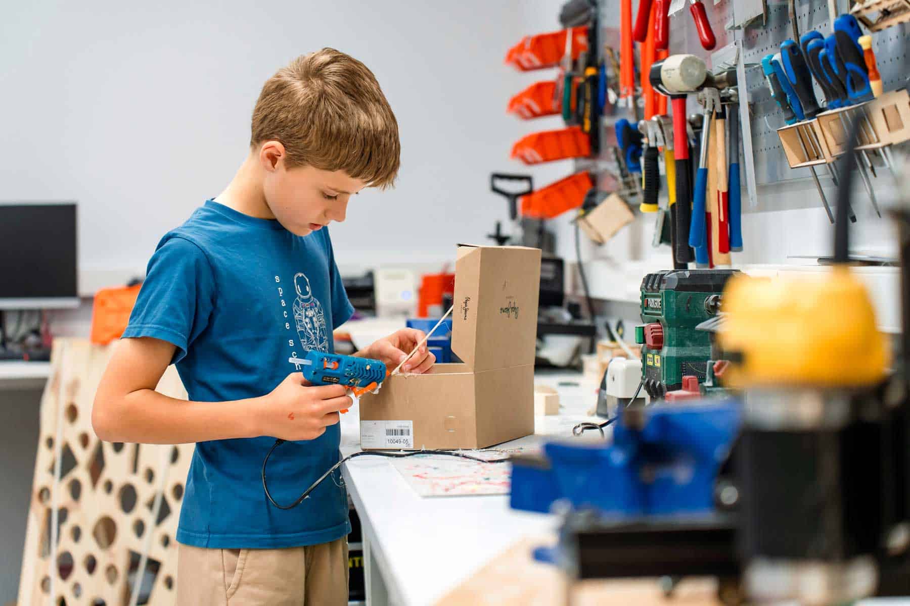 Boy working on DIY project with glue gun in workshop, learning practical skills at World Schools.