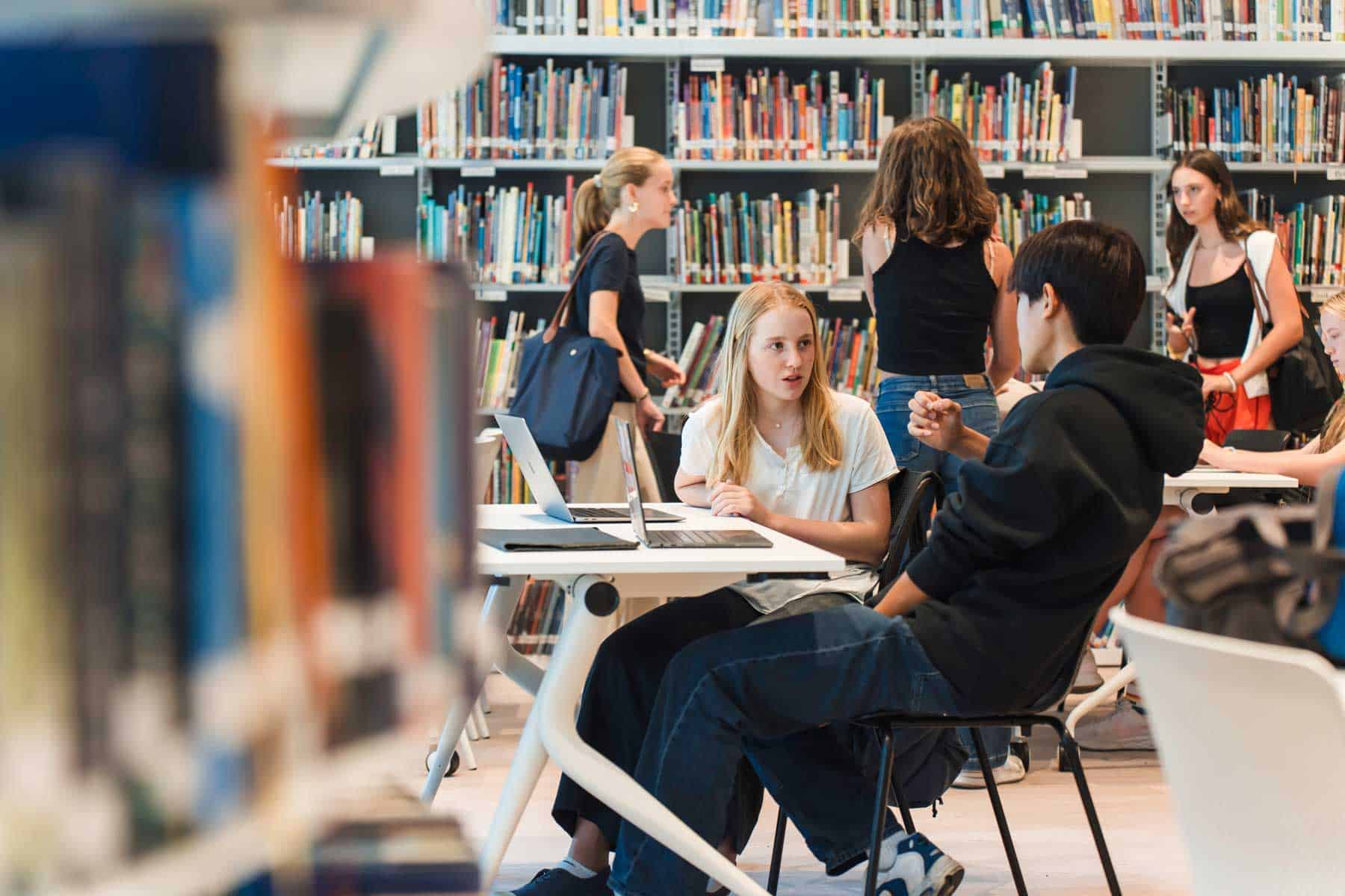 Brightly lit school library with students studying and chatting, emphasizing a modern educational environment.