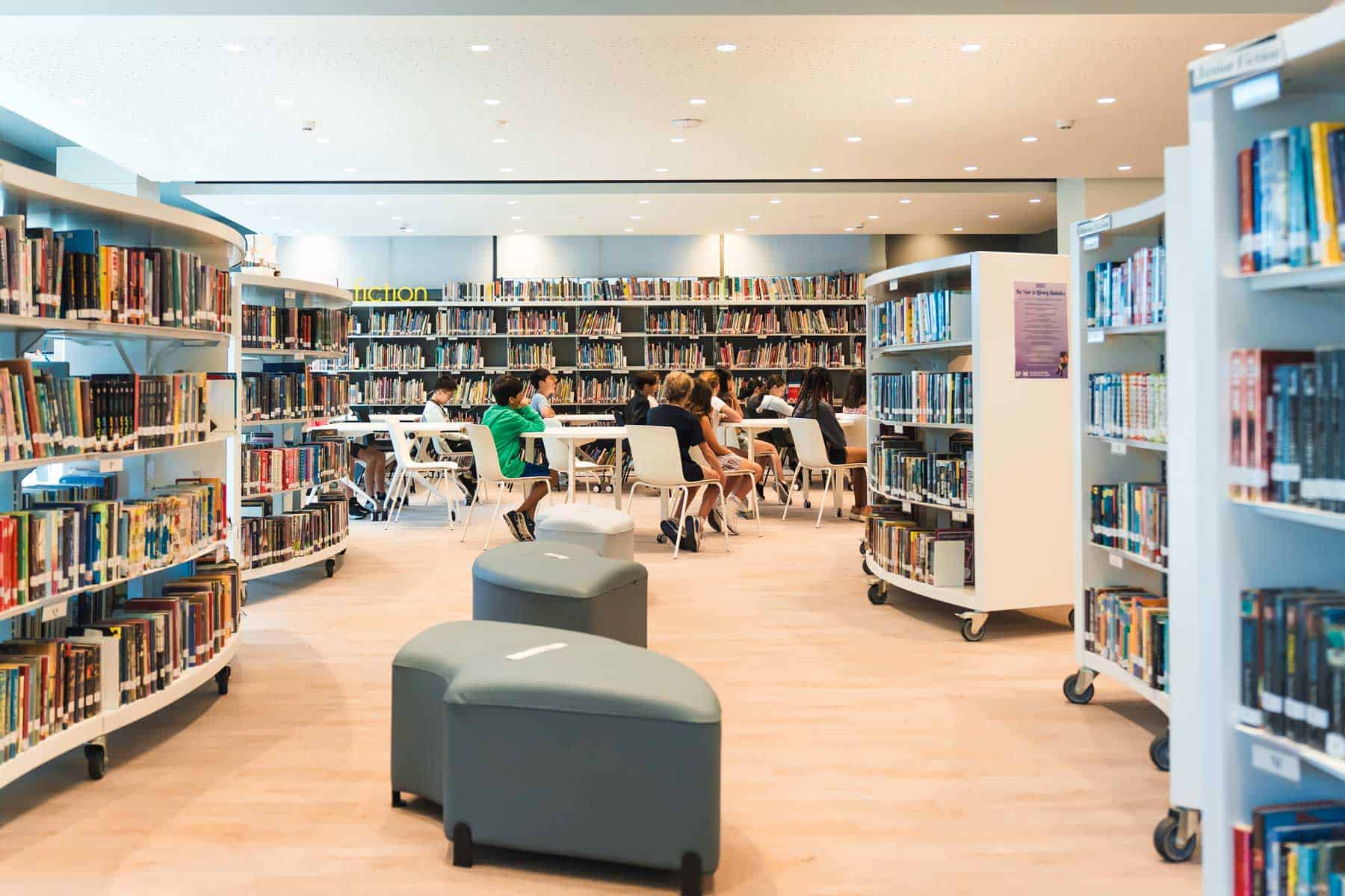 Bright library filled with students studying and reading in a modern educational environment.