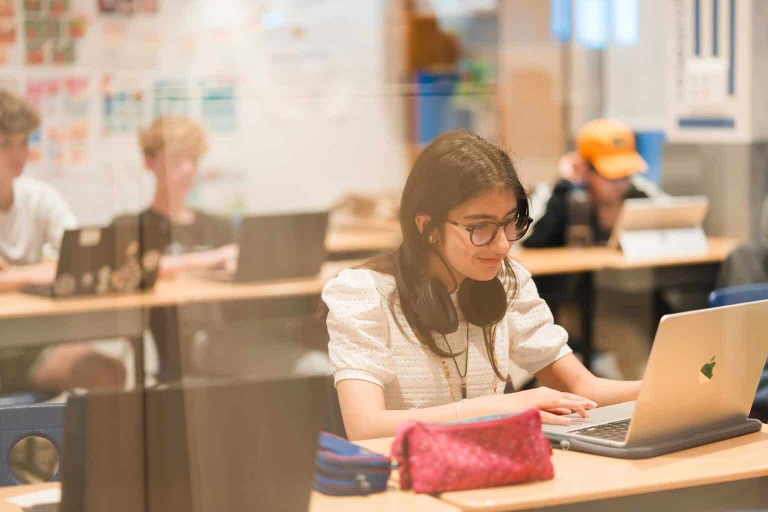 Young girl studying with laptop and headphones in a modern classroom.