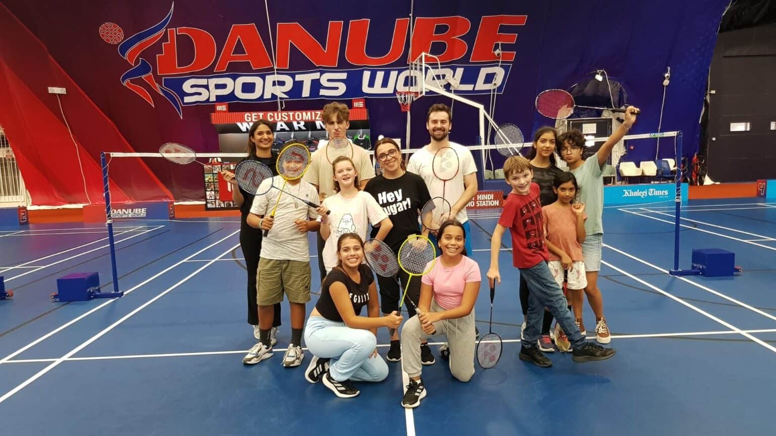 Indoor badminton court with a diverse group of children and coaches posing after a game.