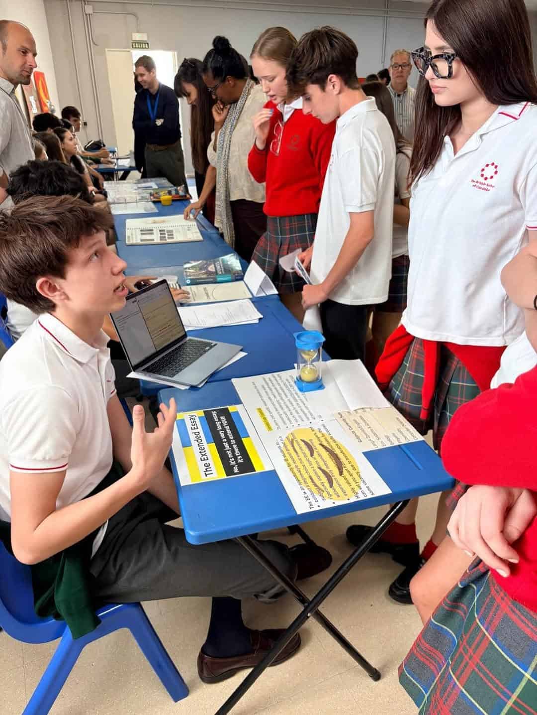 Students presenting science project at school fair with teachers and peers.
