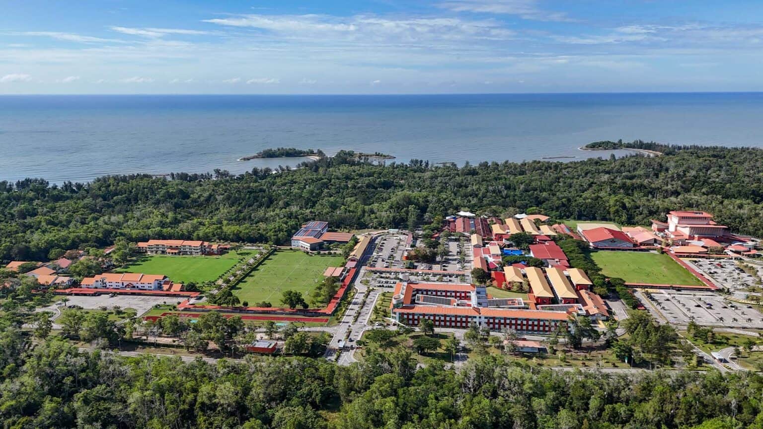 Lush green and red-roofed educational campus with ocean view, modern buildings, and sports fields at a world-class school.