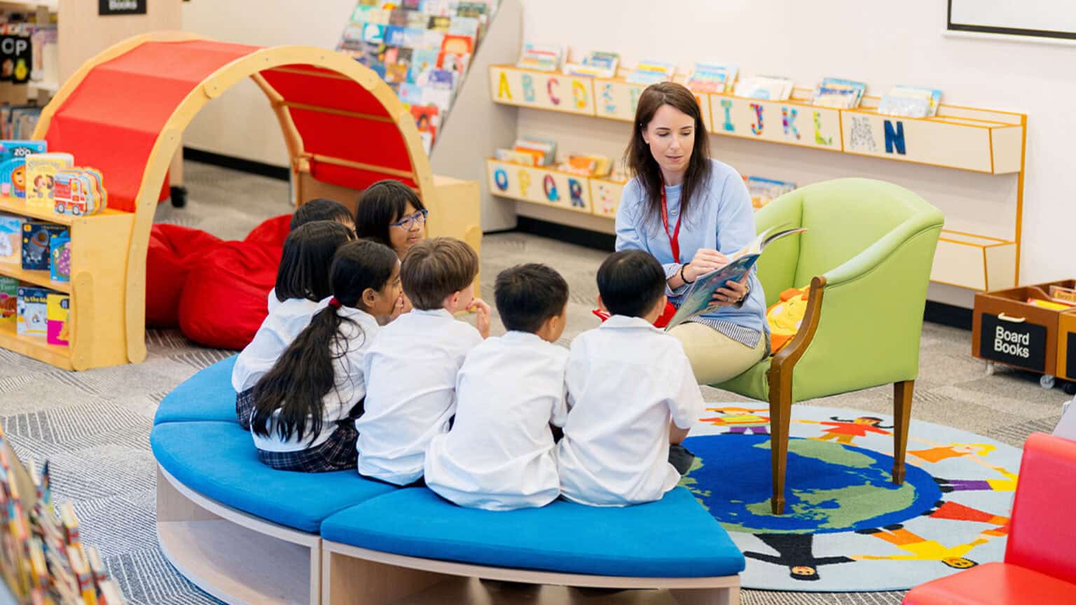 Children engaged in reading with a teacher in a colorful, modern classroom setting for global school education.