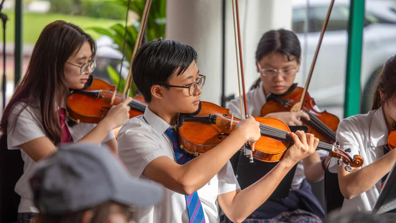 Focused Asian students playing violins during school music class or concert.