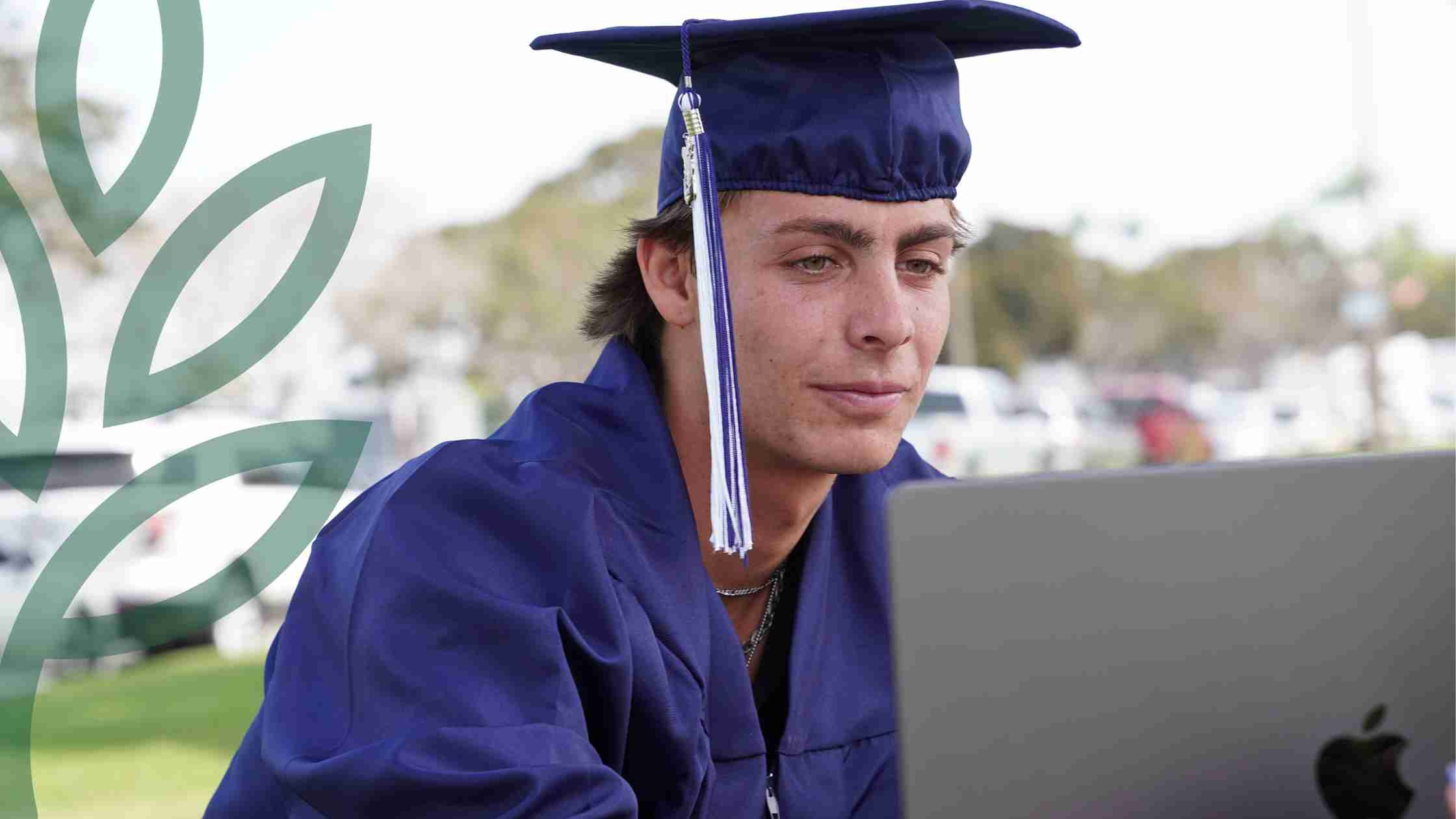 Graduate in cap and gown working on laptop outdoors at World Schools.