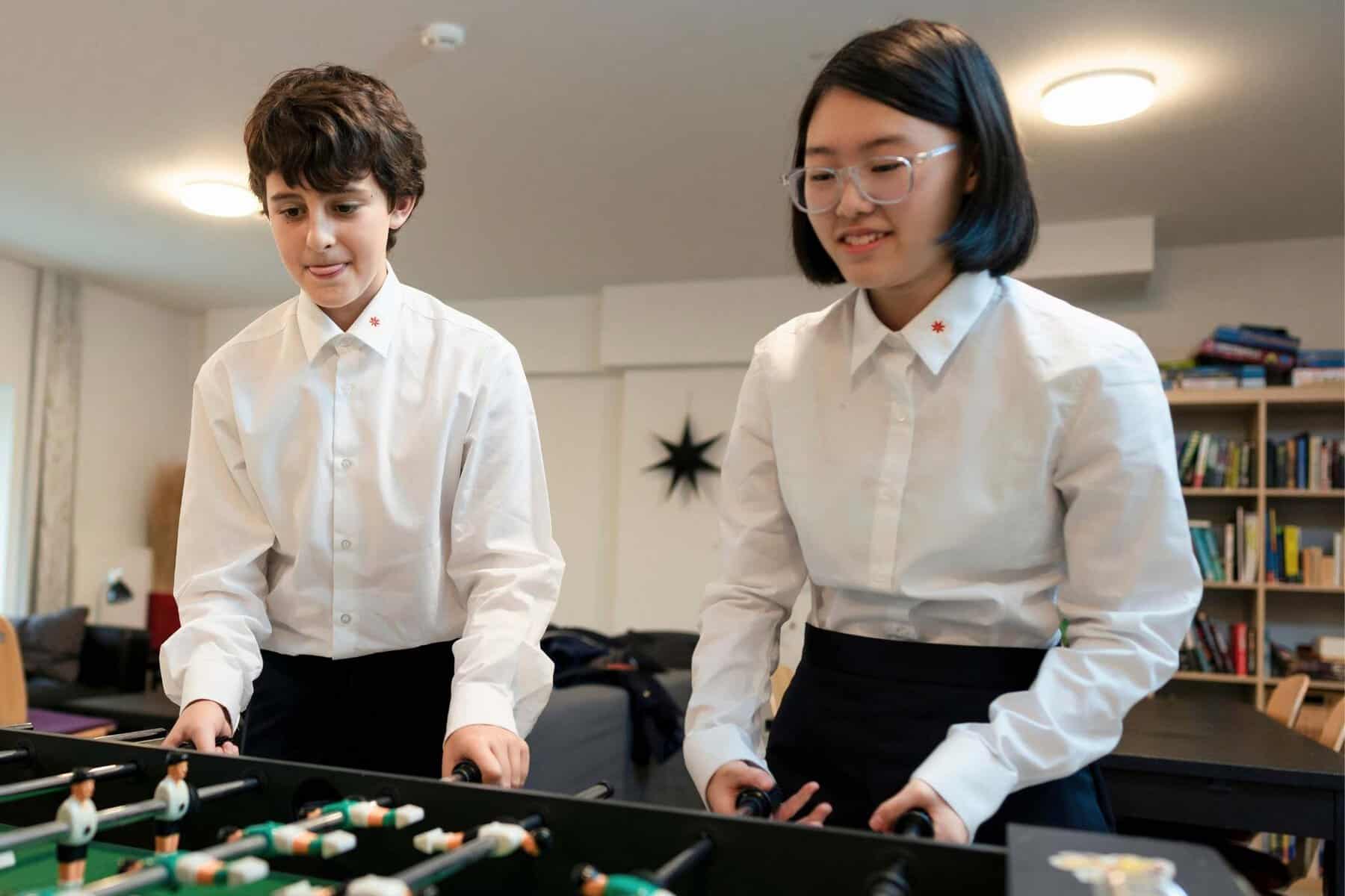 Two diverse students enjoying foosball in a classroom setting.