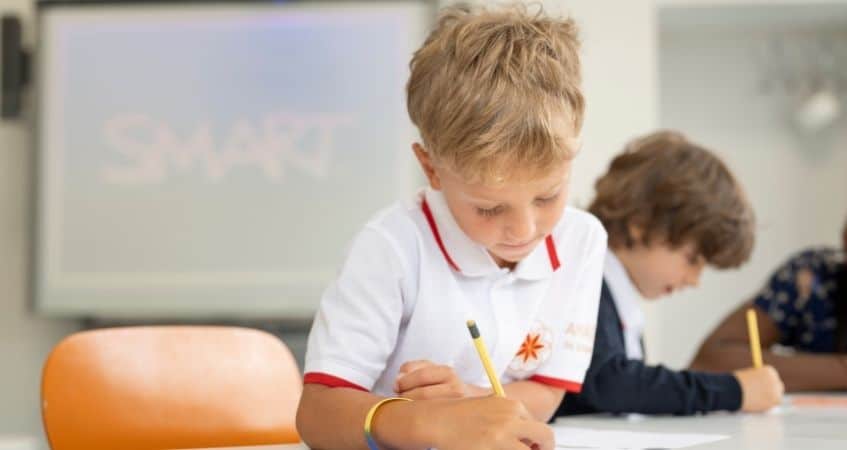 Young children focused on writing in a classroom setting at a world school.