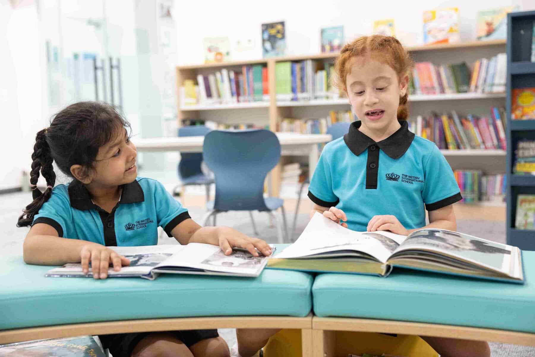 10 Simple Ways to Support Your Child’s Reading at Home 4 Two young students in blue uniforms reading books in a school library.
