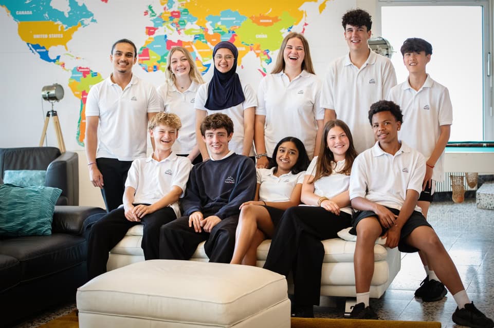 Diverse group of students and teacher smiling in classroom with world map background.