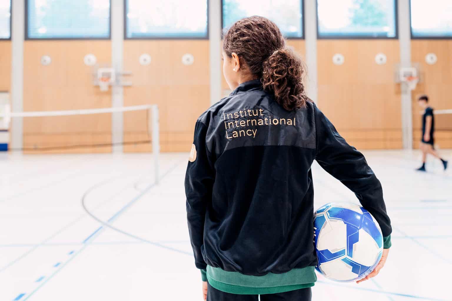Young girl holding a soccer ball in indoor sports facility at Institut International Lancy.