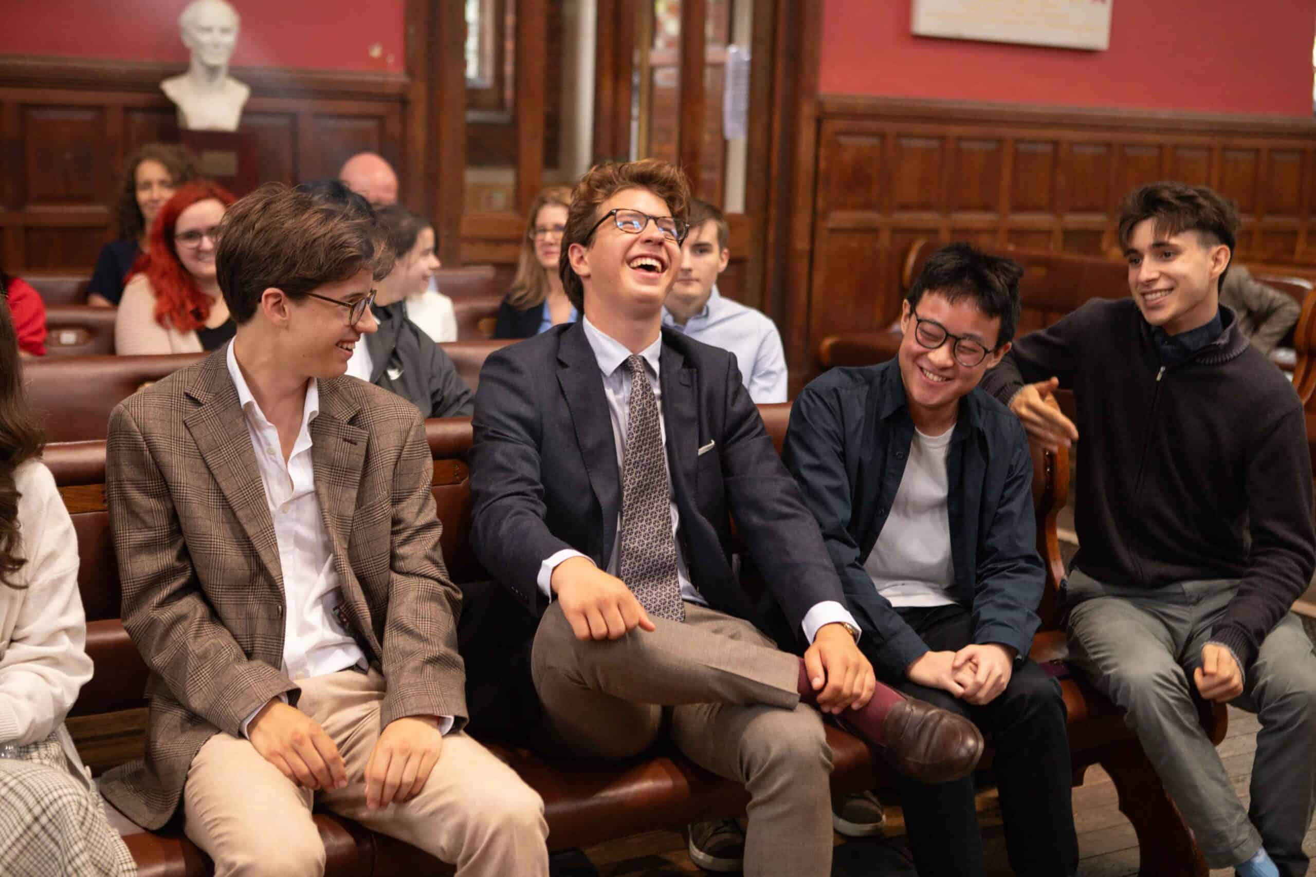 Lively students laughing and enjoying a classroom discussion in a prestigious school hall.