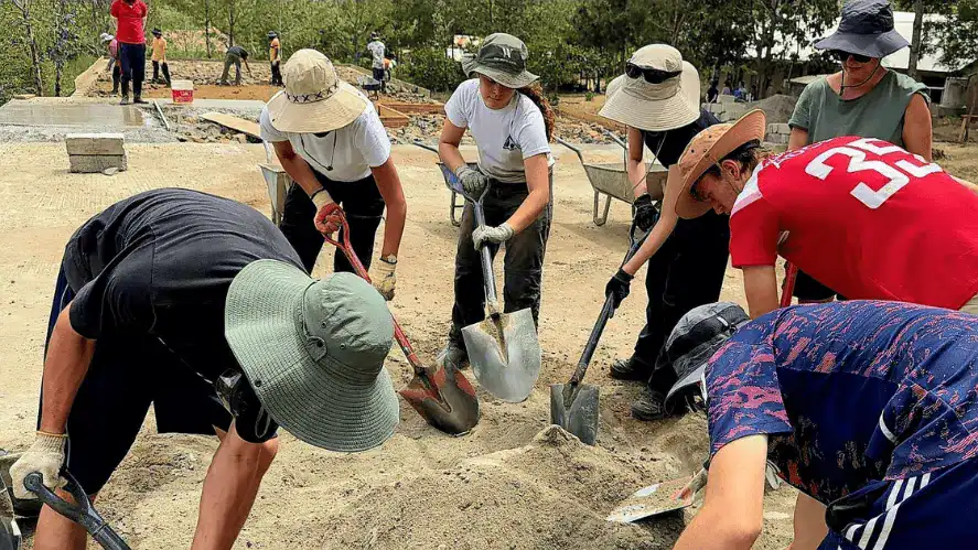 Group of diverse students wearing hats and gloves, collaborating on a construction project outdoors.