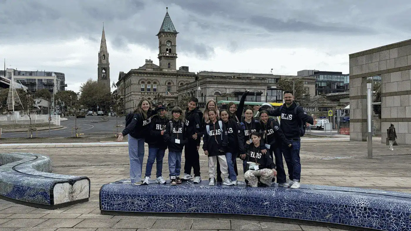 Students in matching hoodies posing in a city square with historic buildings.