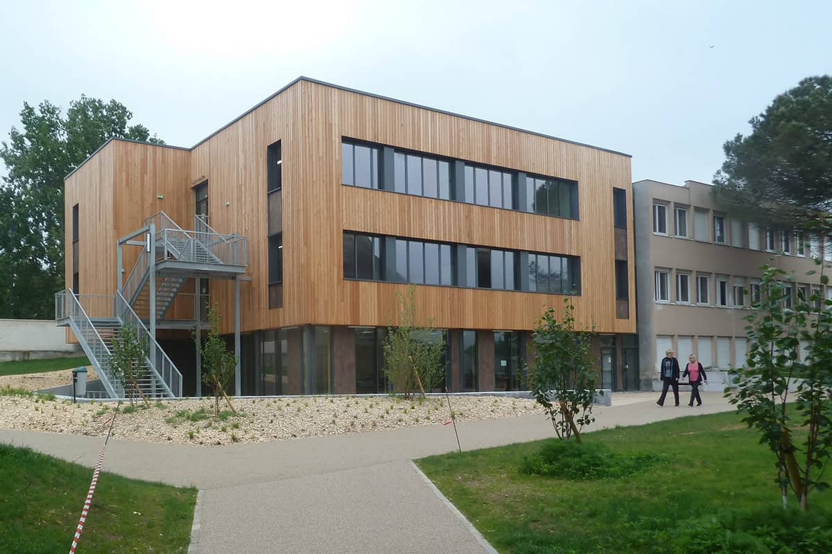 Modern wooden facade school building with large windows and outdoor staircase, promoting innovative education environments.