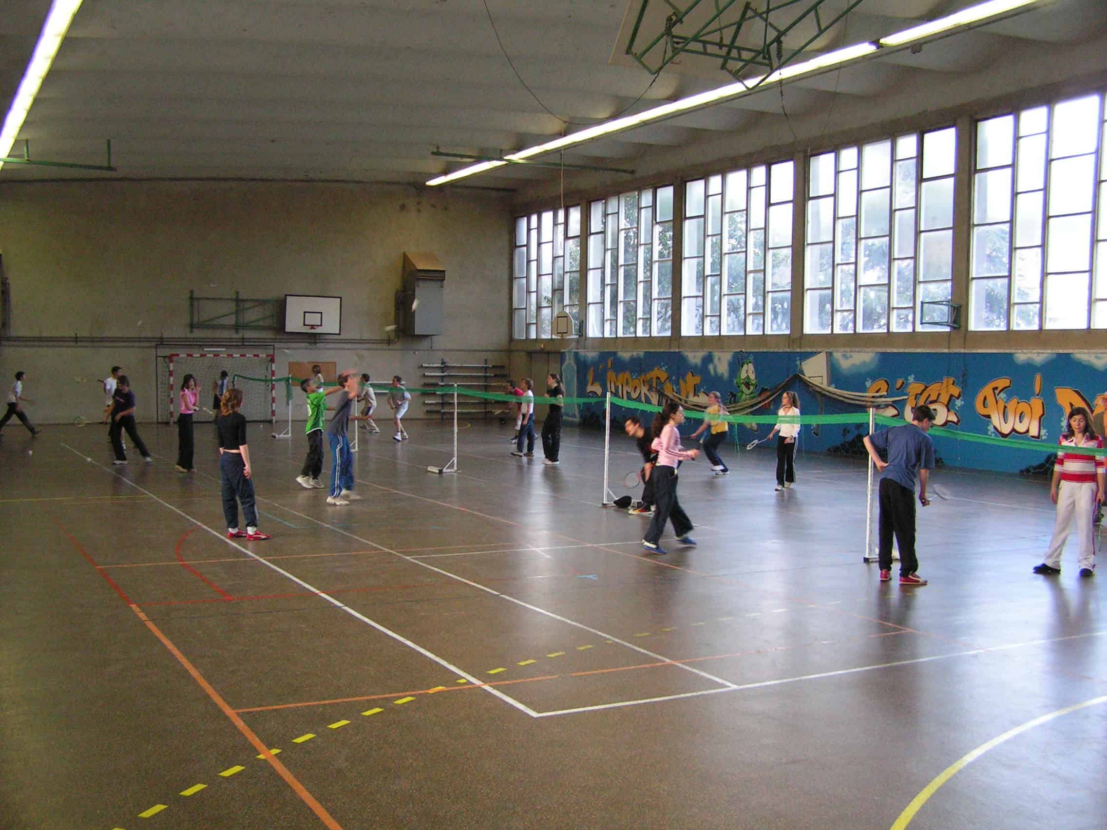Students playing badminton in a school gymnasium for sports education and active lifestyle.