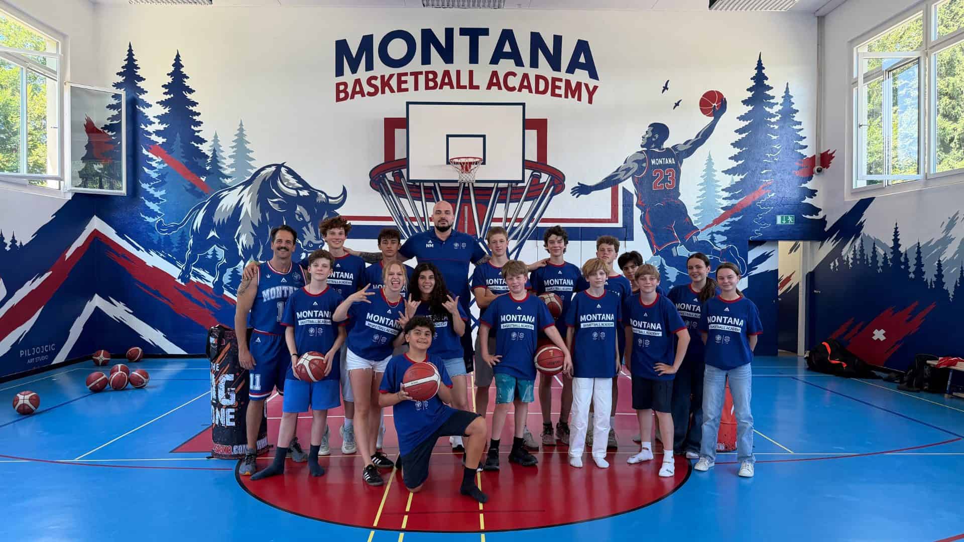 Group photo of Montana Basketball Academy team in gym with mural background.