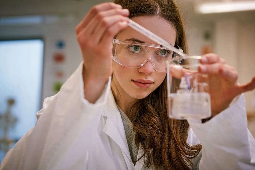 Science student conducting chemistry experiment with test tubes and safety goggles.