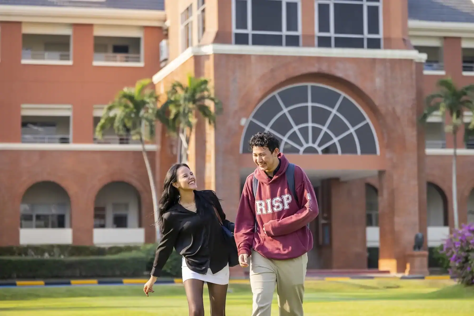 Students walking and talking on campus with modern buildings in the background.