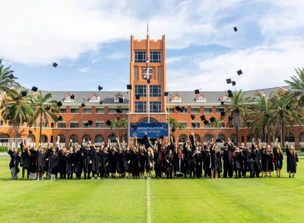 Graduates celebrating at World Schools with caps in the air and a historic building in the backdrop.