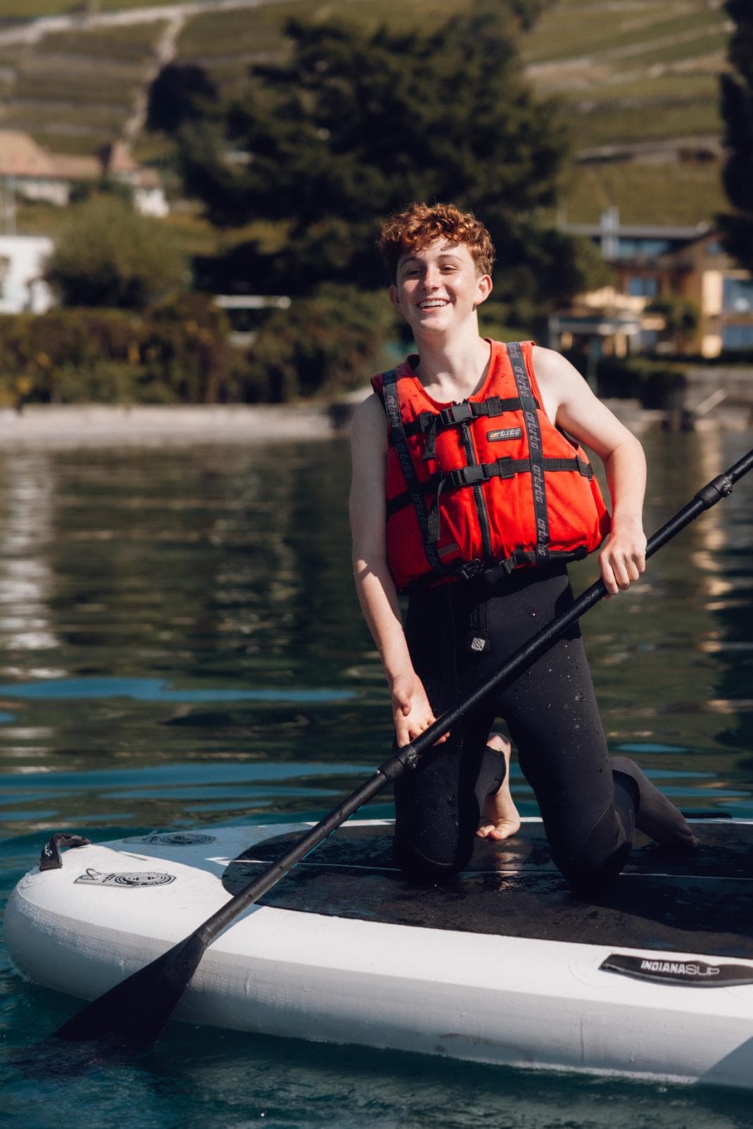 Young boy paddleboarding on a calm lake with scenic hillside background at a world school outdoor activity.
