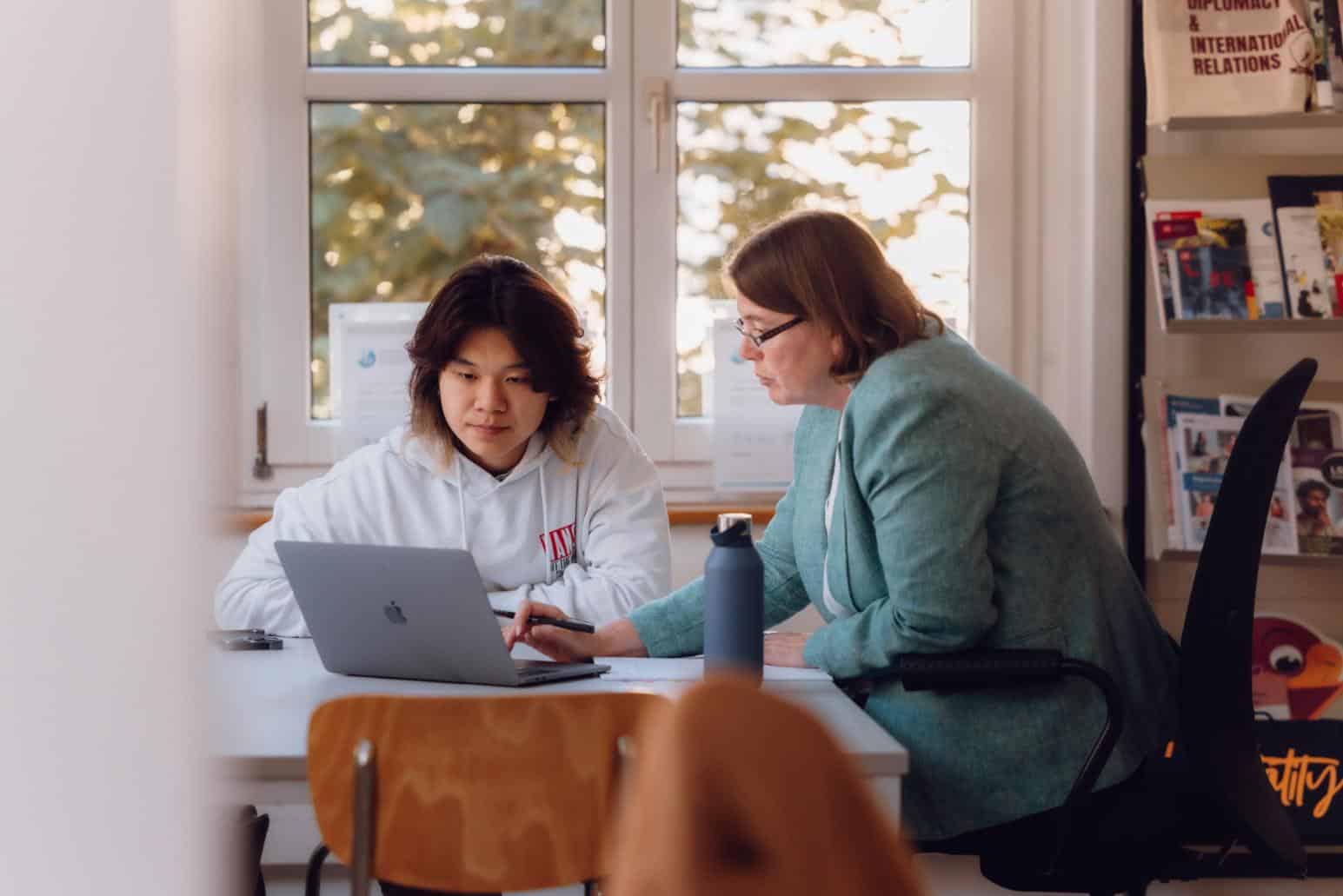 Seated student and teacher collaborating over laptop in classroom at World Schools.