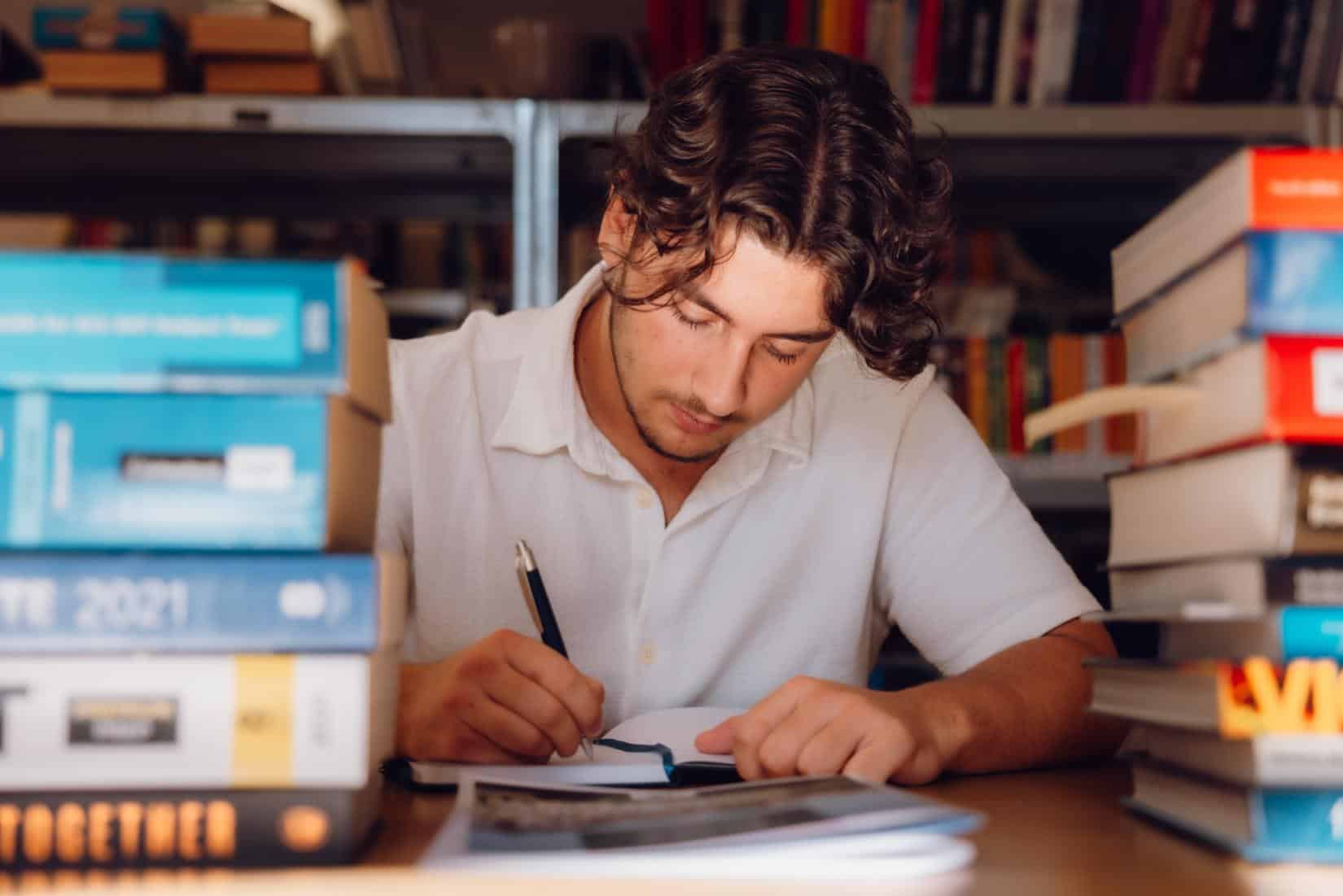 Young student studying with books and notes at library, focused on academic success.