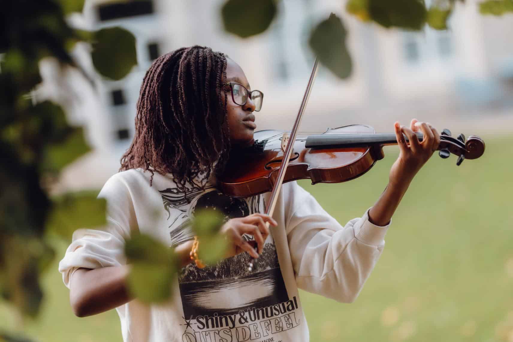 Young girl playing violin outdoors at a school green space, promoting arts education and extracurricular activities.