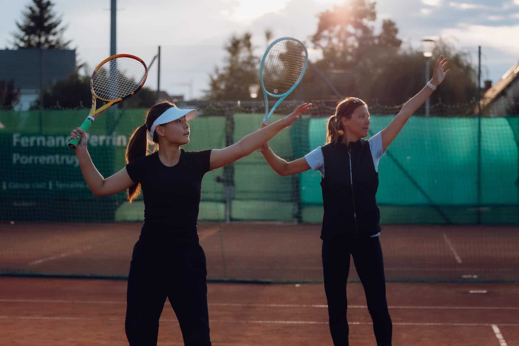 Young female tennis players practicing on outdoor court at sunset, promoting sports education and physical activity.