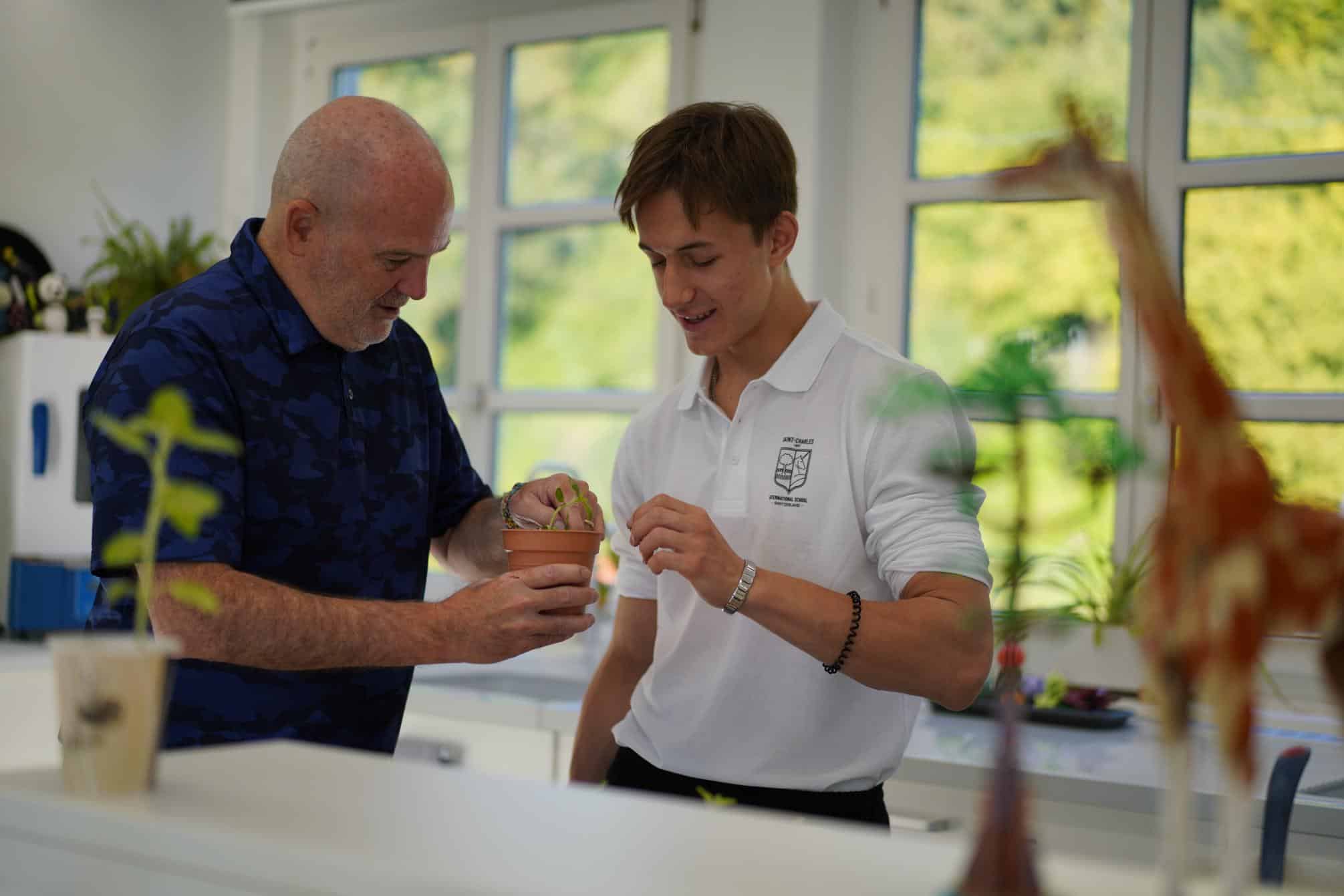 1. Two students examining a potted plant in a science classroom at World Schools.