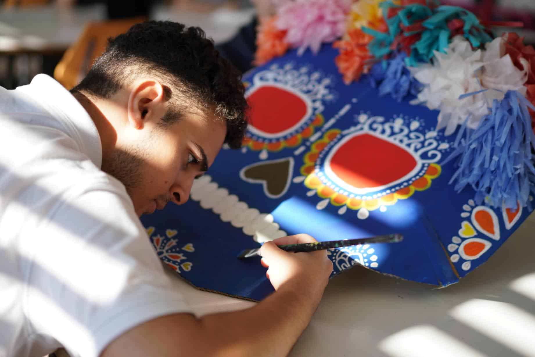 Colorful Mexican Lotería game being decorated by a young man representing cultural education and traditional games for schools.