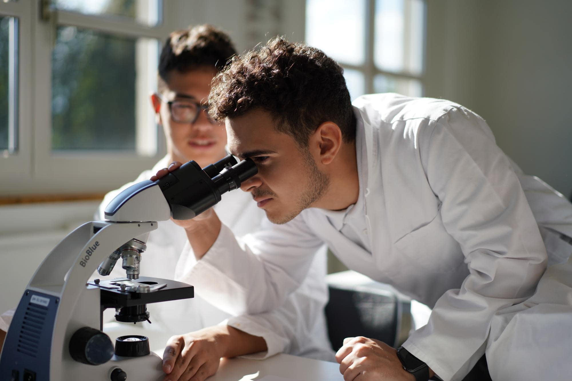 Focused male student examining sample through microscope in science lab.